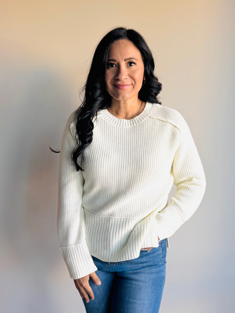 Flatlay of ivory raglan sleeve sweater showing knit texture and side slit design