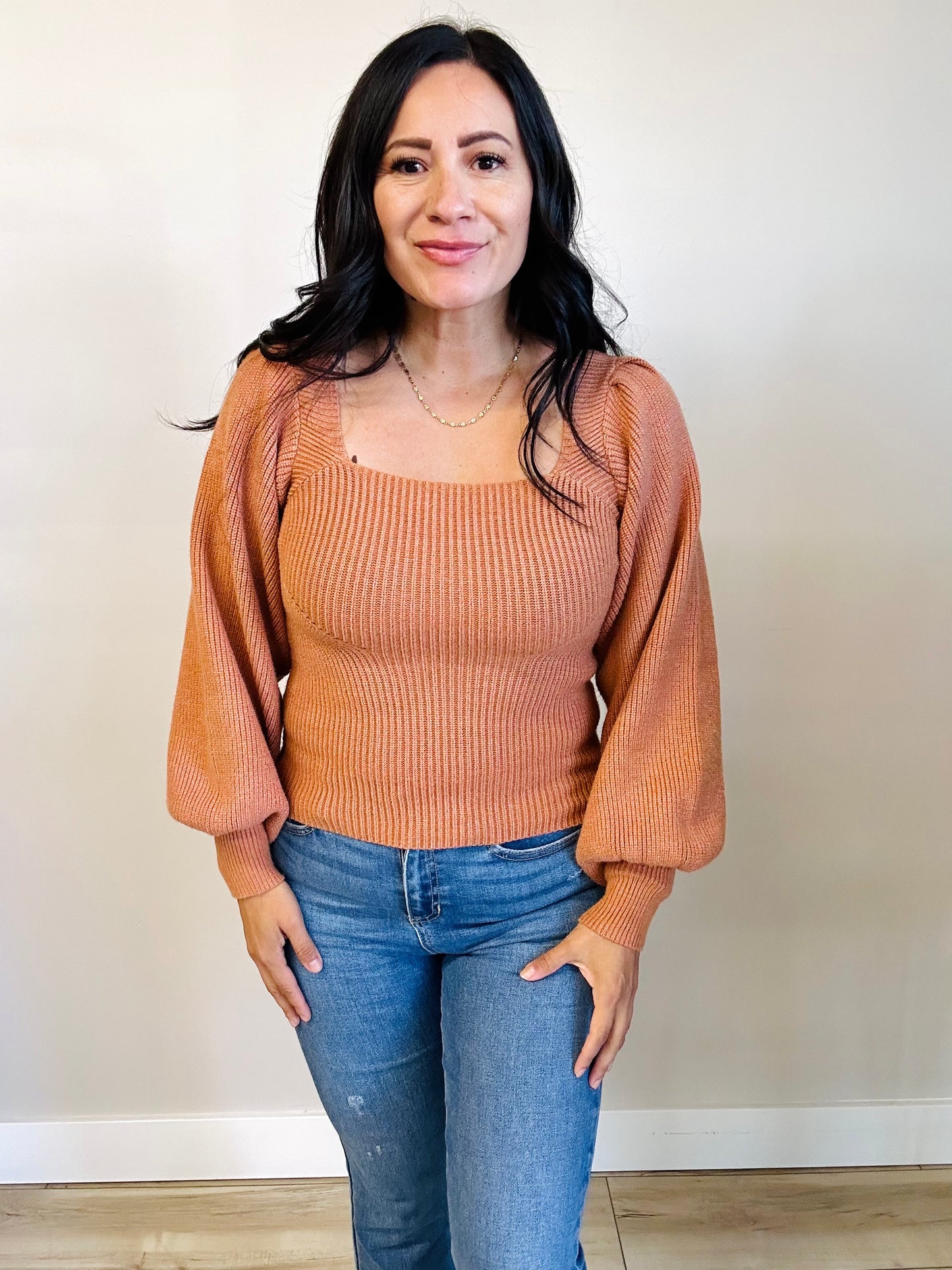 Woman wearing a brown ribbed sweater and blue jeans against a plain background