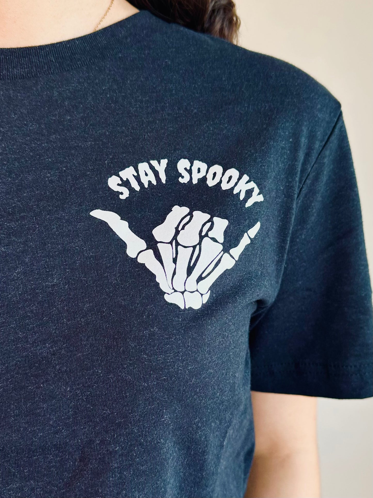 Close-up of Stay Spooky Graphic Tee – white skeleton hand shaka print
