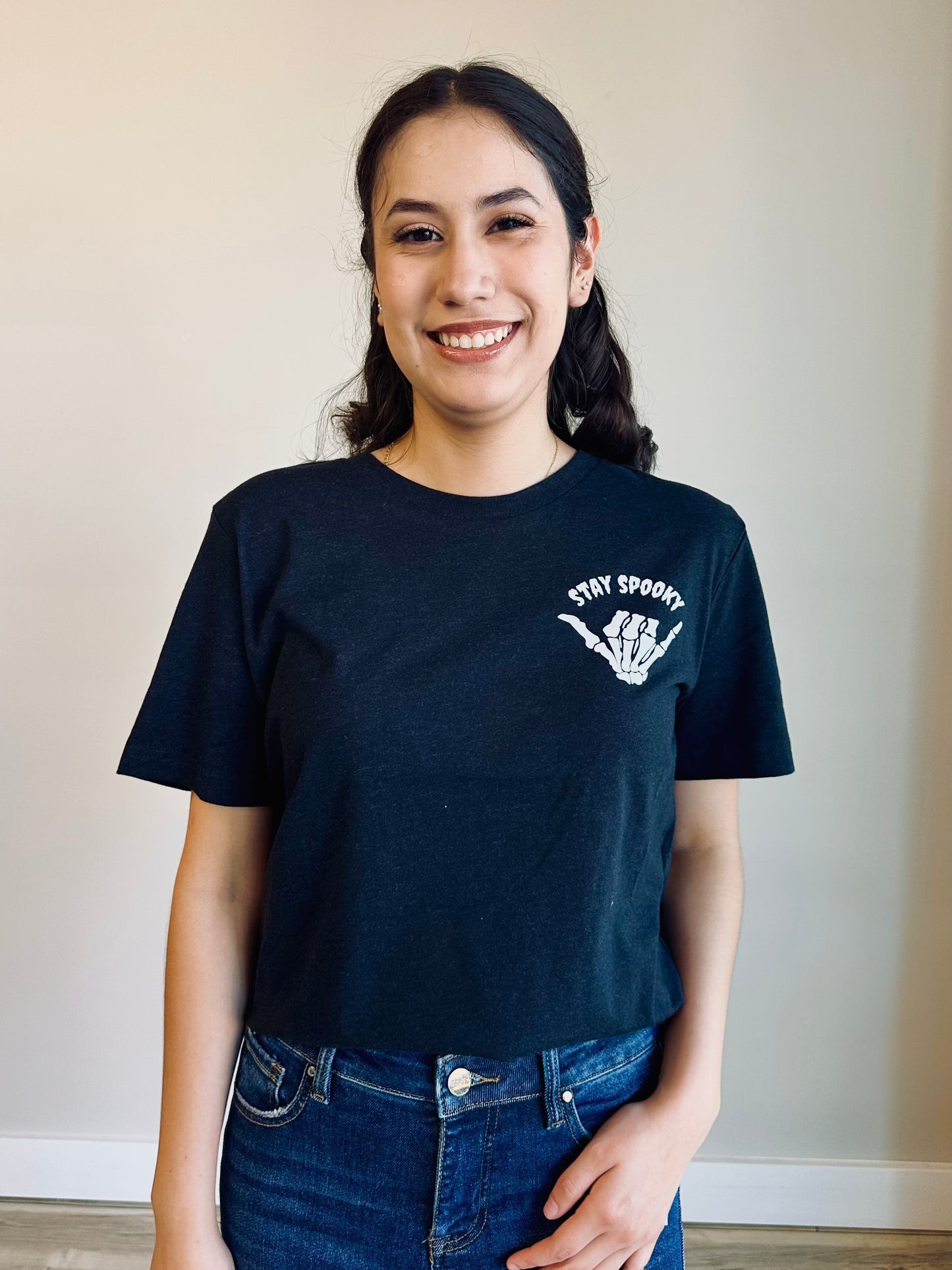 Stay Spooky Graphic Tee front view – black with skeleton hand shaka design